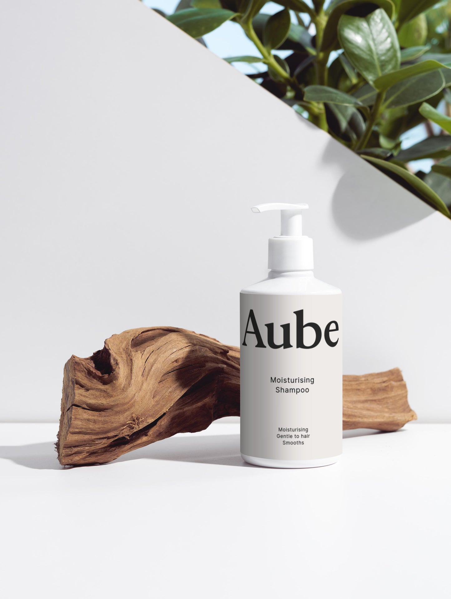 Flacon de shampooing hydratant Aube posé sur un morceau de bois naturel avec une plante en arrière-plan, sur fond blanc minimaliste.